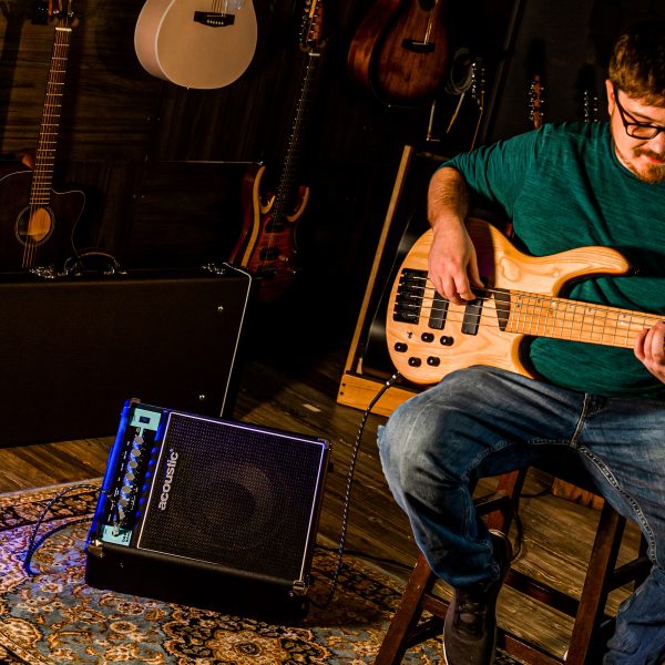 a bass guitar player performing with B25C combo bass amp in a room full of guitars