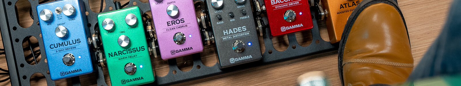 Six Gamma guitar pedals on pedal board next to guitar player: Cumulus, Narcissus, Eros, Hades, Bacchus, and Atlas